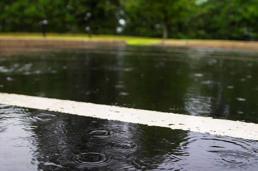 a wet road with rain droplets creating ripples on the water.