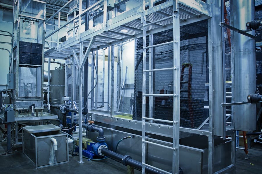 En el entorno de una fábrica se instala una compleja disposición de equipos y maquinaria industrial compuesta por armazón metálico, tuberías y bombas.