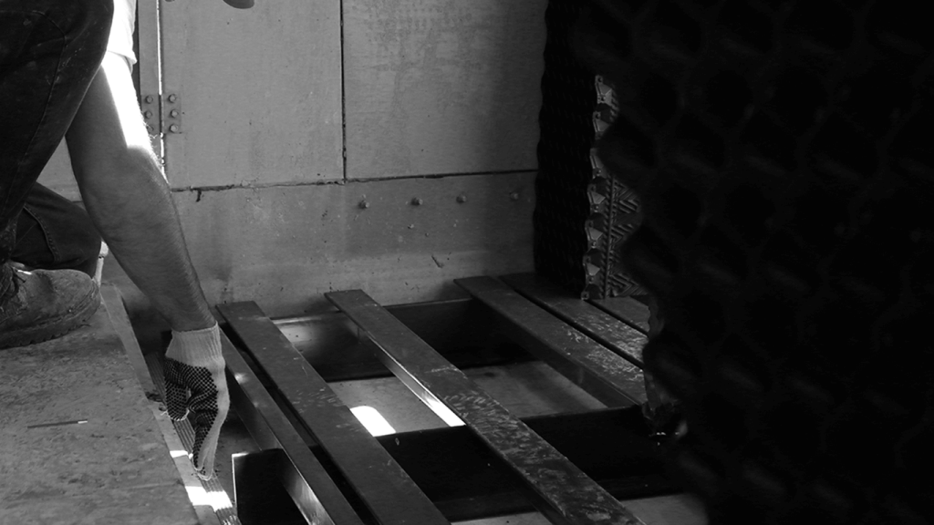 A person with, wearing gloves, is kneeling by metal beams at a construction site. The background reveals a partially constructed wall.