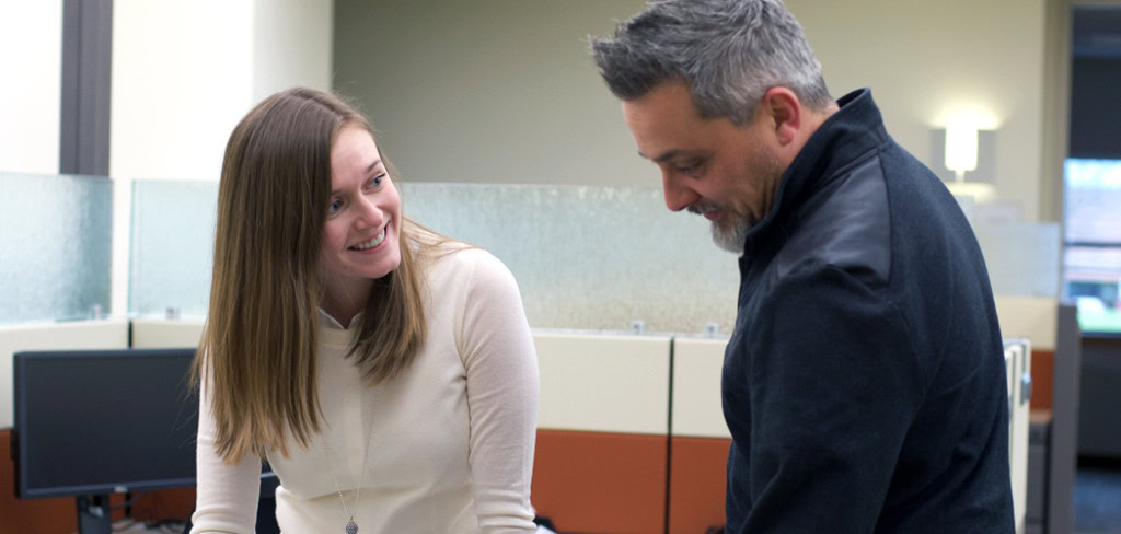 A woman with long hair and a man with short hair and a beard are smiling and engaged in conversation.