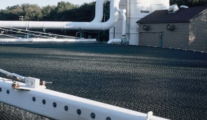 A large industrial facility with extensive pipework and a grated structure in the foreground showcasing a trickling filter.