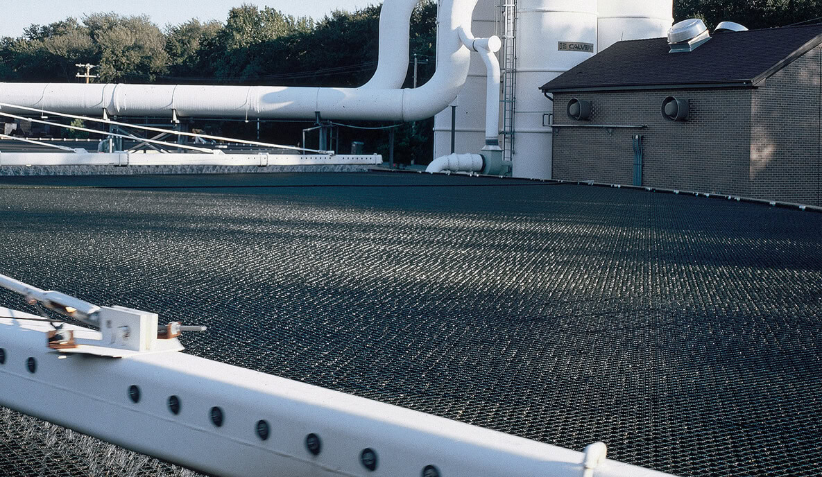 A large industrial facility with extensive pipework and a grated structure in the foreground showcasing a trickling filter.