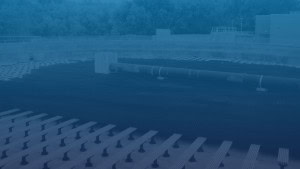 An overhead view of an industrial facility featuring several large pipes and concrete structures. The image has a blue tint.
