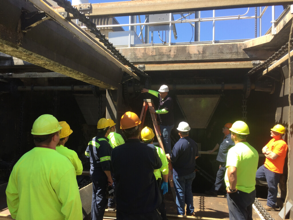 Person standing inside a wastewater clarifier, giving instructions to staff nearby.